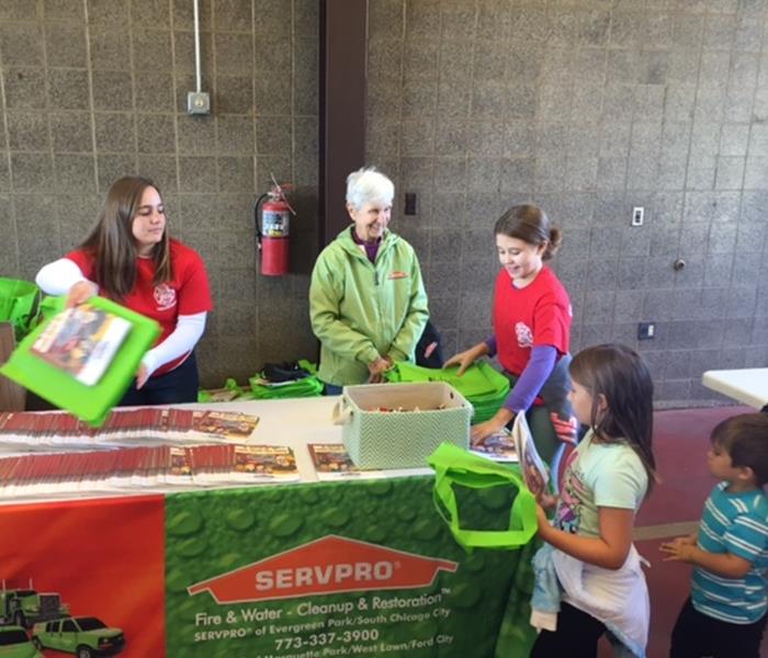 two females at a desk handing SERVPRO promotional items to 3 children