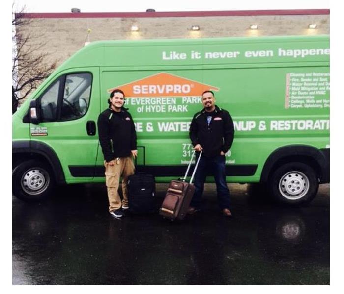 two male employees standing in front of a green SERVPRO van