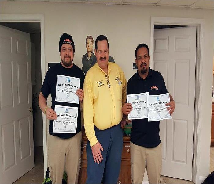 two SERVPRO employees holding certificates standing with a water damage restoration trainer
