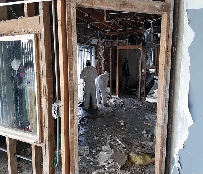 living room with drywall removed and two employees picking up debris littering the floor