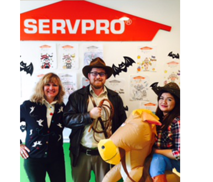 three people dressed up in halloween costumes in front of a SERVPRO sign